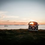 Vintage camper van parked by the ocean at sunset.
